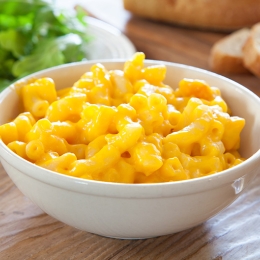 Bowl of macaroni and cheese with bread and salad in background