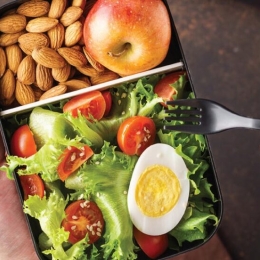 box of food with a salad, egg, almonds, and apple